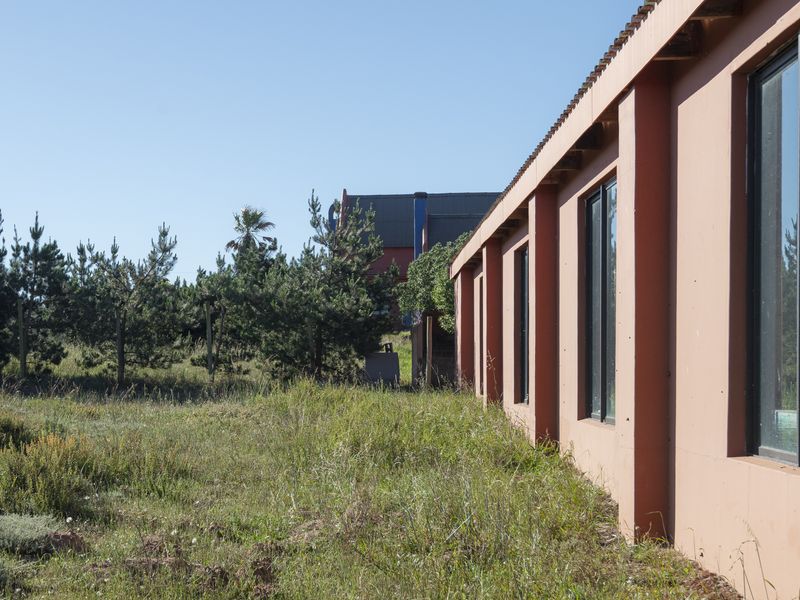 Rear exterior view of the farm property featuring terracotta-colored walls, large windows, and overhanging eaves, set against a natural landscape.