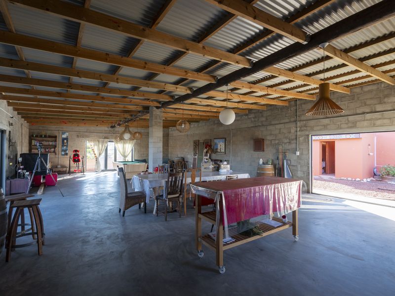 Spacious open-plan living area featuring exposed timber roof trusses, concrete block walls, and polished concrete floors with large sliding doors opening to the exterior.