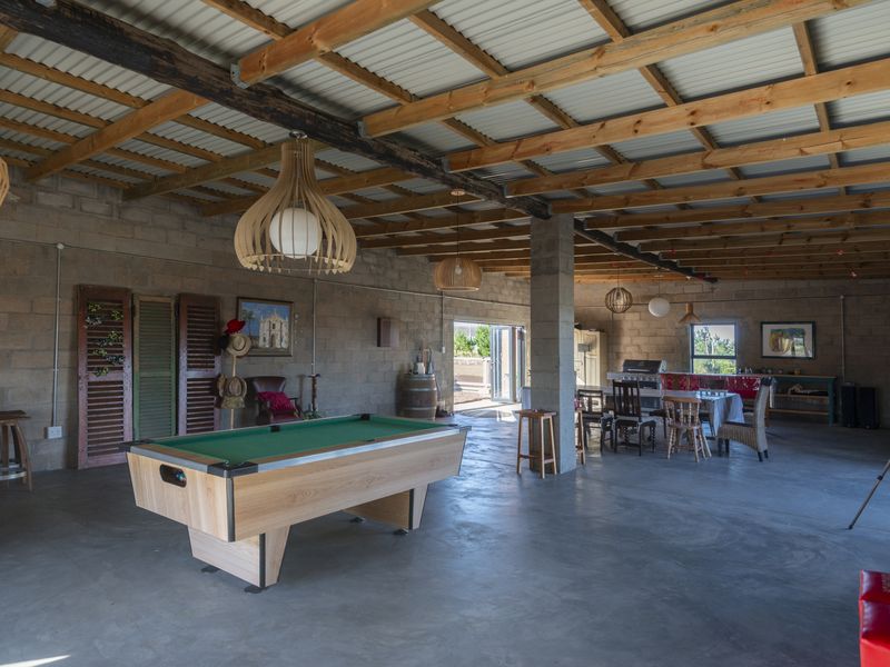 Spacious open-plan living area featuring exposed timber roof trusses, concrete block walls, and polished concrete floors, offering a versatile entertainment space.