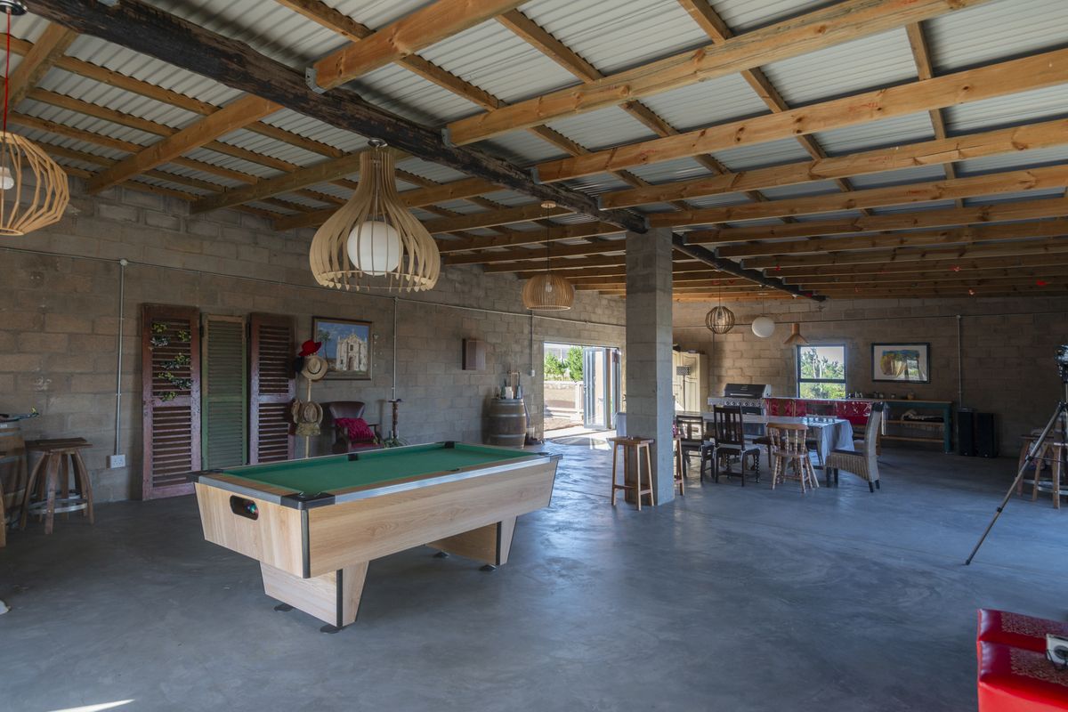 Spacious open-plan living area featuring exposed timber roof trusses, concrete block walls, and polished concrete floors, offering a versatile entertainment space.