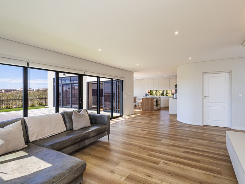 Spacious open-plan living area featuring modern laminate flooring, recessed lighting, and seamless flow to the outdoor patio through large sliding glass doors.