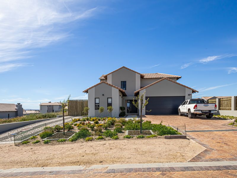 Modern double-story residential home featuring a paved driveway, double garage, and well-maintained front garden under a clear blue sky.