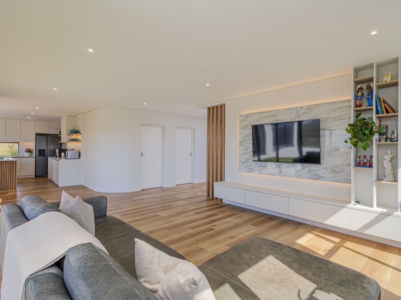 Modern open-plan living area featuring timber flooring, a custom marble-look media wall with integrated shelving, and a sleek, contemporary kitchen with island.