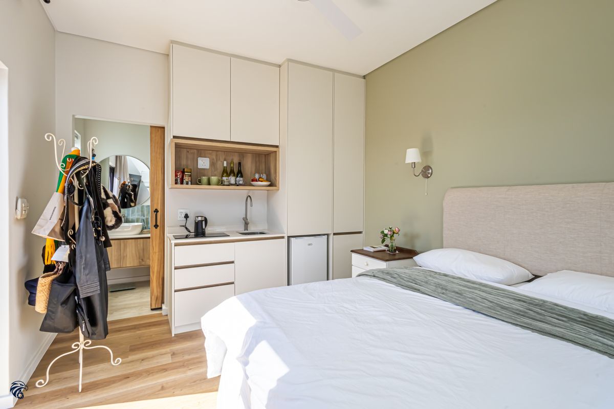 A well-appointed bedroom featuring a compact kitchenette with built-in cabinetry, sink, and hob, complemented by modern laminate flooring and an en-suite bathroom access.