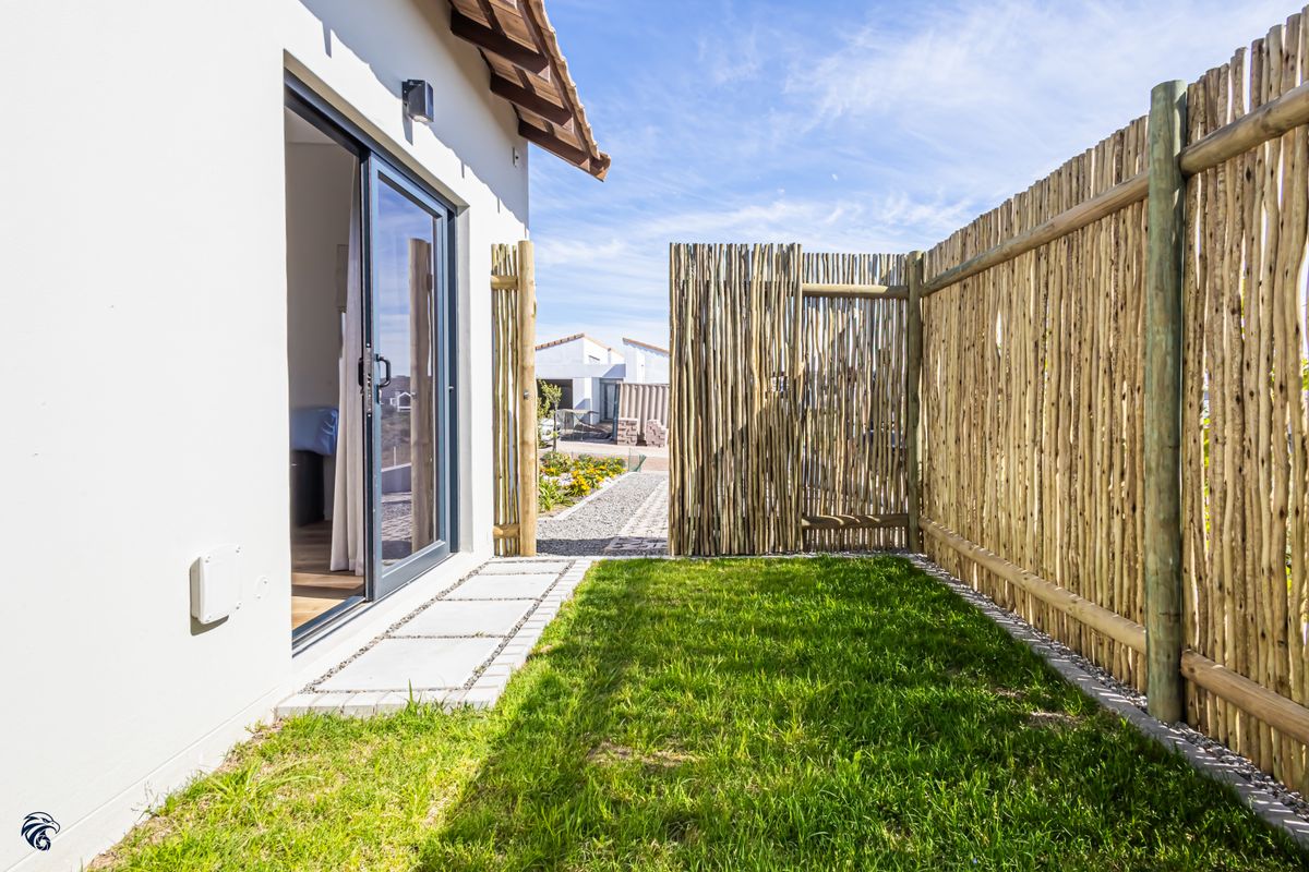A private rear garden area featuring a well-maintained lawn, paved pathway, and natural timber pole fencing, accessible via a modern sliding glass door.
