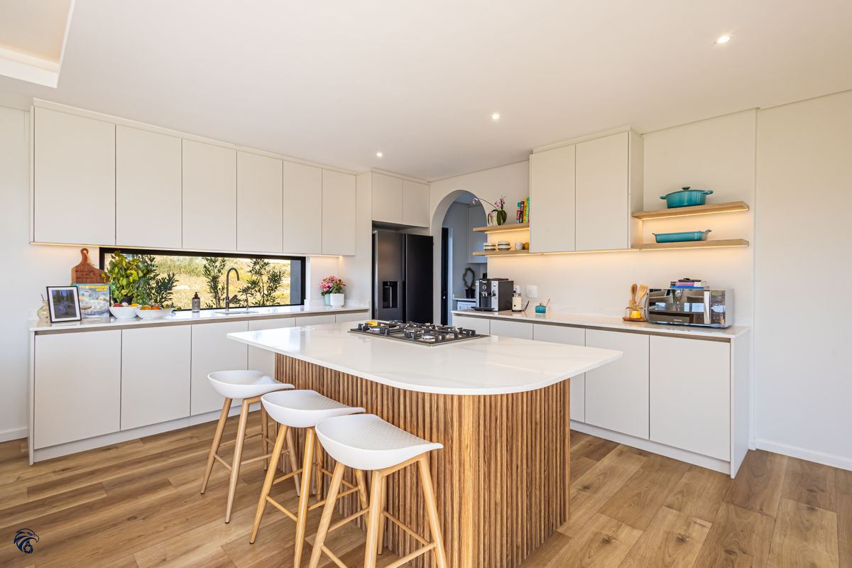 Modern kitchen featuring a central island with gas hob, sleek handleless cabinetry, stone countertops, and integrated appliances, complemented by warm under-cabinet lighting.