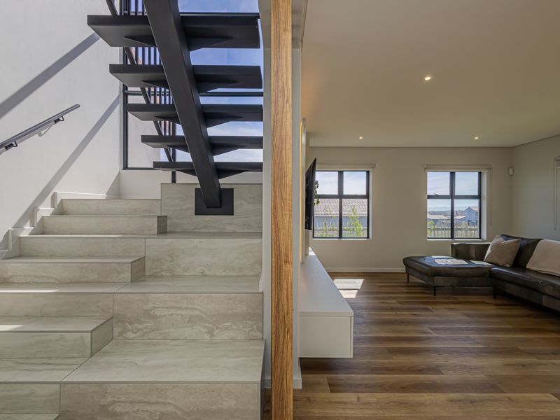Modern open-plan living area featuring a striking floating staircase with stone treads, timber-look flooring, and a sleek built-in media console.