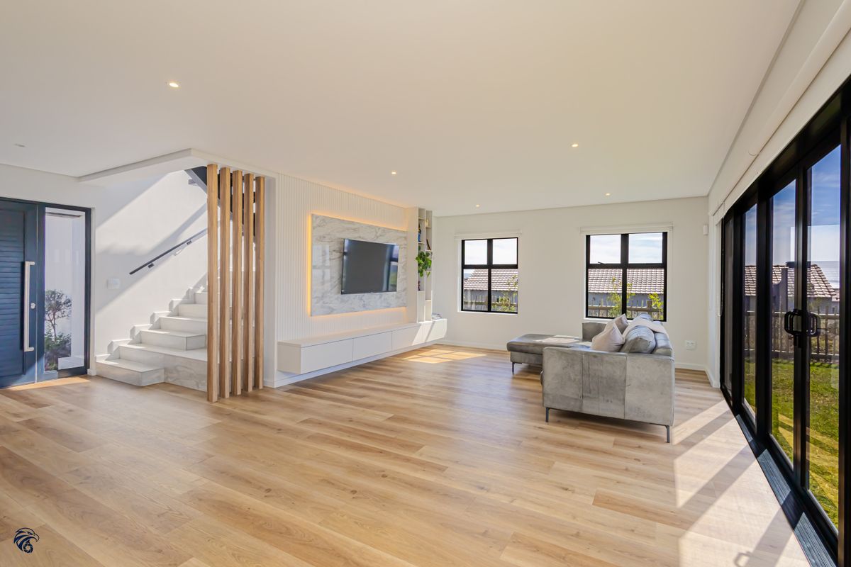 Modern open-plan living area featuring a marble-clad media wall, timber staircase with slat detailing, and large sliding doors leading to the exterior.