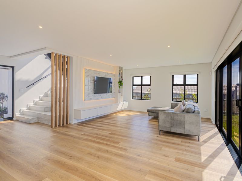 Modern open-plan living area featuring a marble-clad media wall, timber staircase with slat detailing, and large sliding doors leading to the exterior.