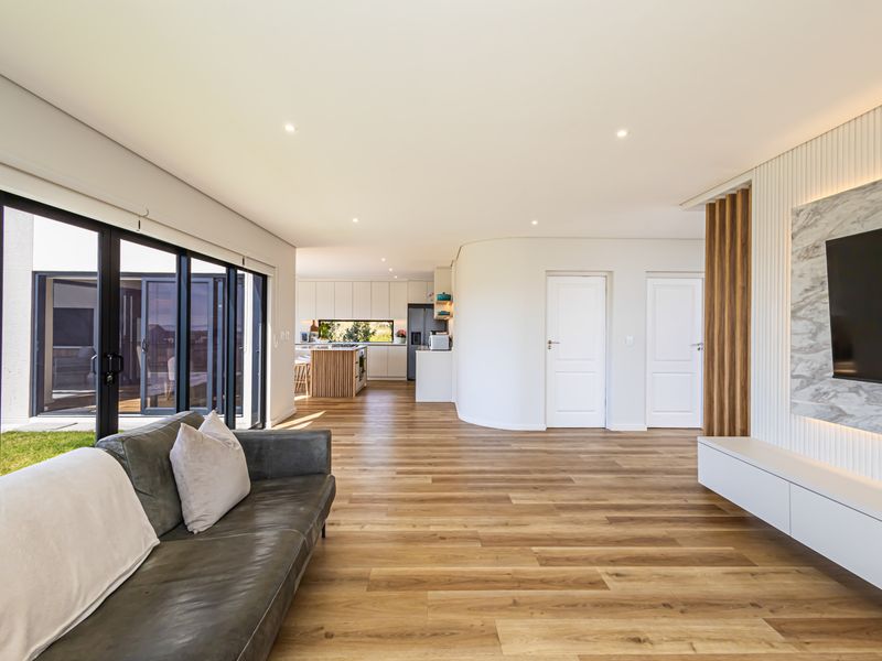 Modern open-plan living area featuring timber flooring, recessed lighting, and a sophisticated media wall with marble accents, seamlessly connecting to a contemporary kitchen.