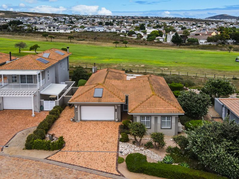 Aerial view of a residential property featuring a terracotta tiled roof, solar panel, paved driveway, and double garage, situated near a golf course.