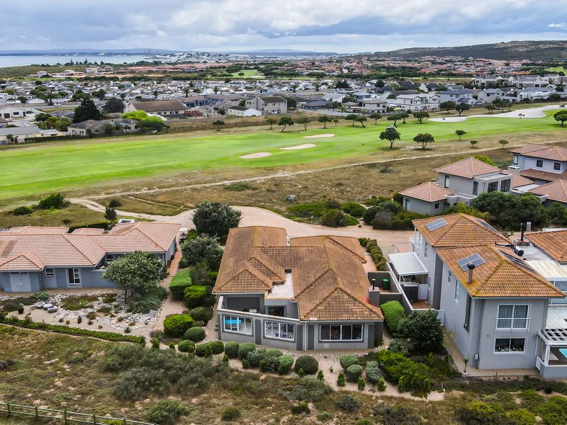 Aerial view of a residential property featuring a tiled roof, solar panels, and landscaped garden, situated in a coastal estate overlooking a golf course.