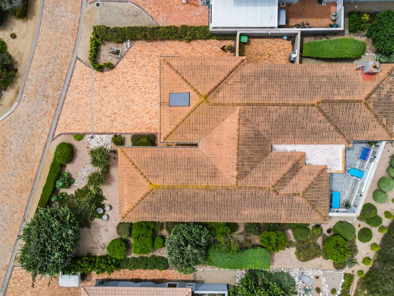 Aerial view of the property showcasing the tiled roof, paved driveway, and surrounding landscaped garden areas.