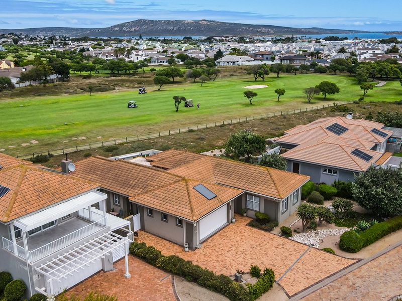 Aerial view of a residential property featuring a tiled roof with solar panels, paved driveway, and balcony, overlooking a golf course.