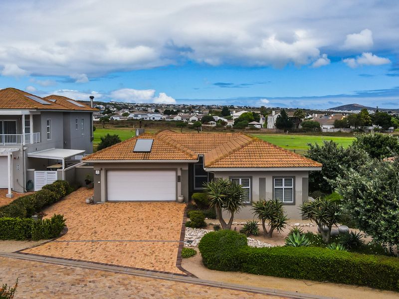 Aerial view of a well-maintained single-story house featuring a tiled roof, brick-paved driveway, garage, and landscaped garden with scenic neighborhood views.