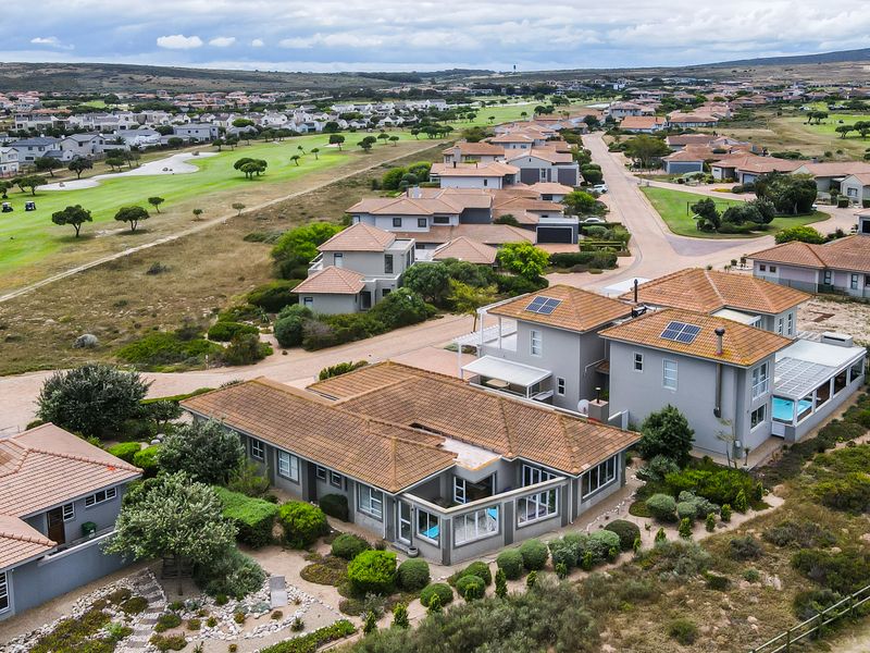 Aerial view of a residential estate featuring modern homes with tiled roofs, solar panels, private swimming pools, and landscaped gardens in a coastal setting.