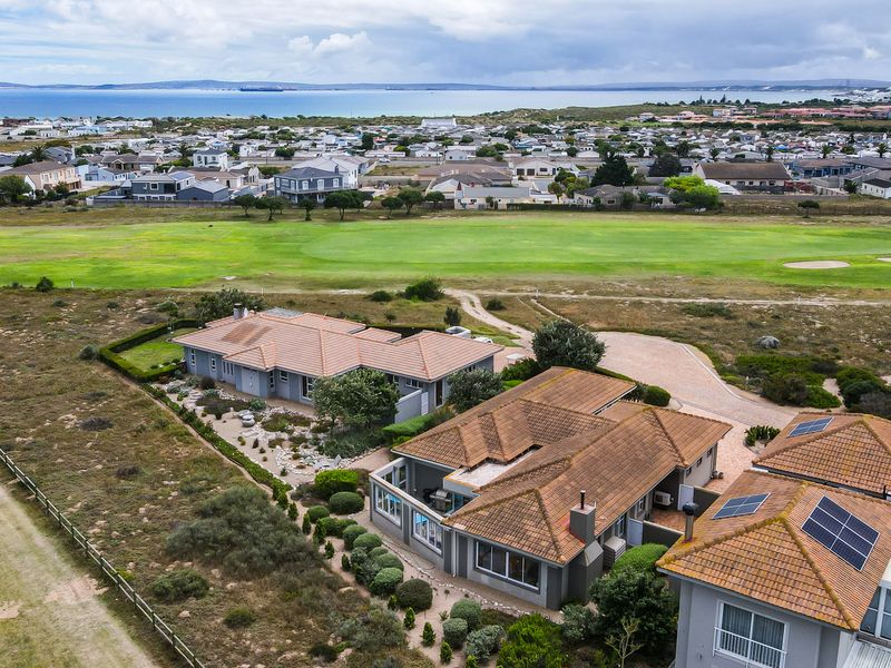 Aerial view of a residential property featuring terracotta tiled roofs, solar panels, and a landscaped garden, situated near a golf course and the coast.