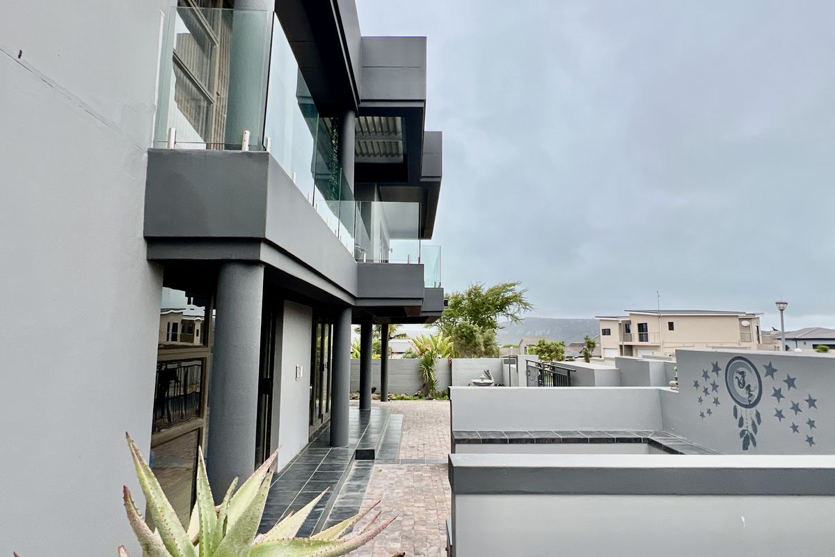 Modern multi-story exterior featuring glass balustrades, dark grey architectural finishes, and a paved patio area.