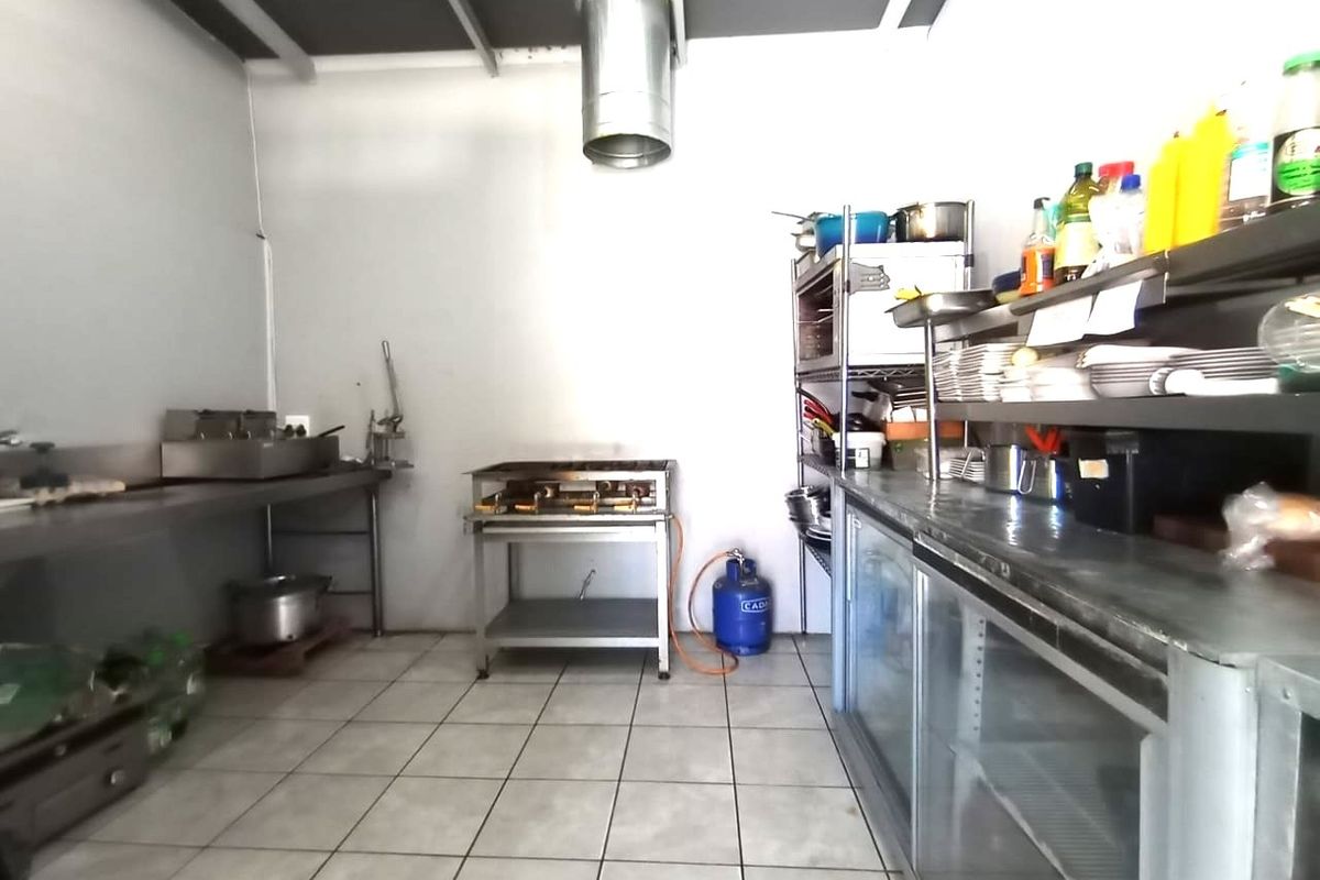 A functional commercial kitchen space featuring stainless steel work surfaces, commercial-grade refrigeration, a gas grill, and an overhead extractor system.