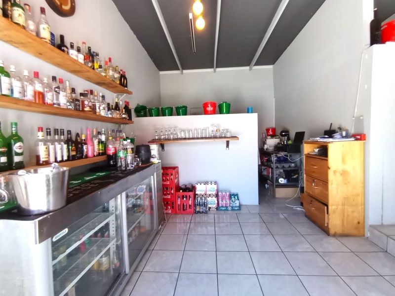 A functional bar area featuring a built-in counter, under-counter refrigeration, floating timber shelving, and tiled flooring.