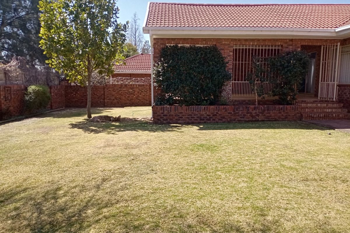 A rear view of the property featuring a face brick facade, tiled roof, security bars on windows, and a private garden with a brick boundary wall.