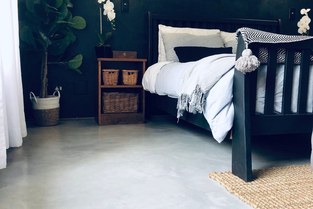 A modern bedroom featuring polished concrete flooring, dark accent walls, and contemporary pendant lighting.