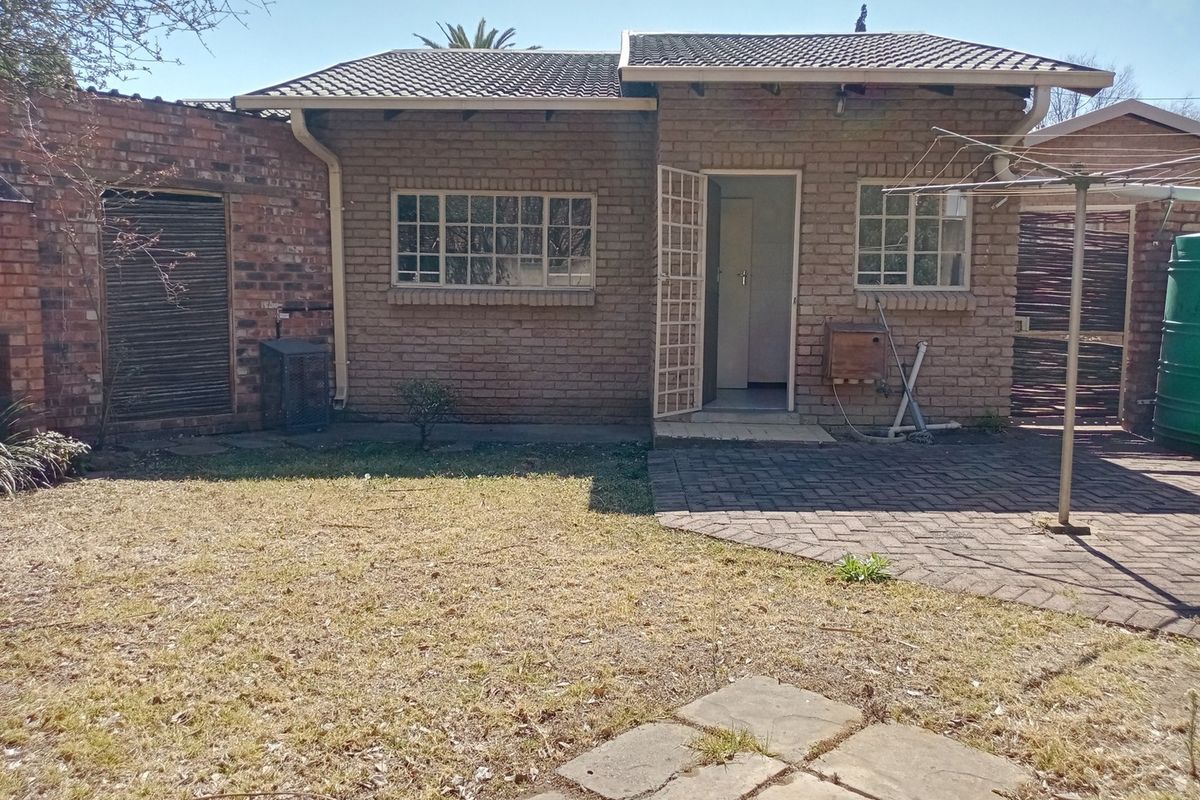 Rear view of a brick townhouse featuring a paved patio area, small garden, and security gate access.