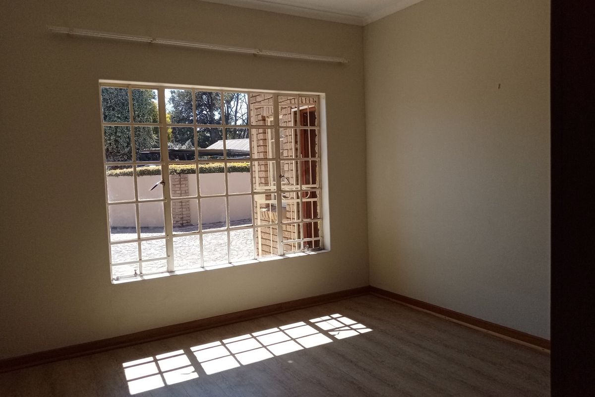 A bright, empty bedroom featuring large grid-style windows, neutral walls, and wood-look flooring, offering a clean canvas for personalization.