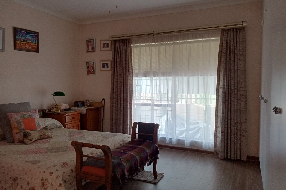 A well-maintained bedroom featuring laminate flooring, a large window with curtain treatments, and a ceiling fan.