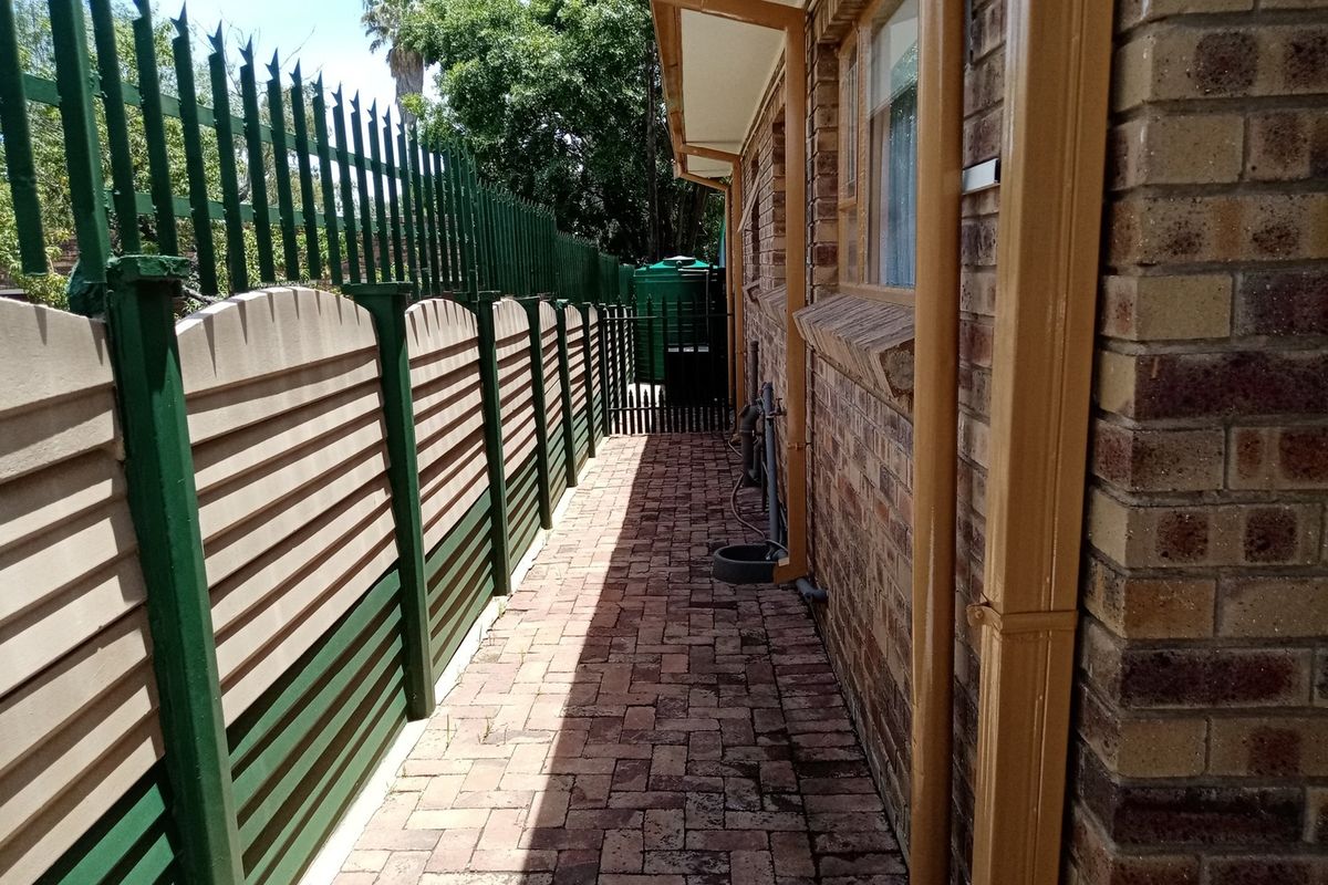 A side exterior walkway featuring brick paving, a secure metal perimeter fence, and a water storage tank located at the rear of the property.