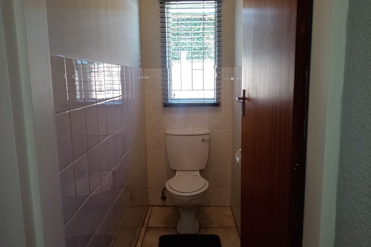 A compact, functional guest toilet featuring ceramic wall and floor tiling, a window with blinds, and a solid timber door.