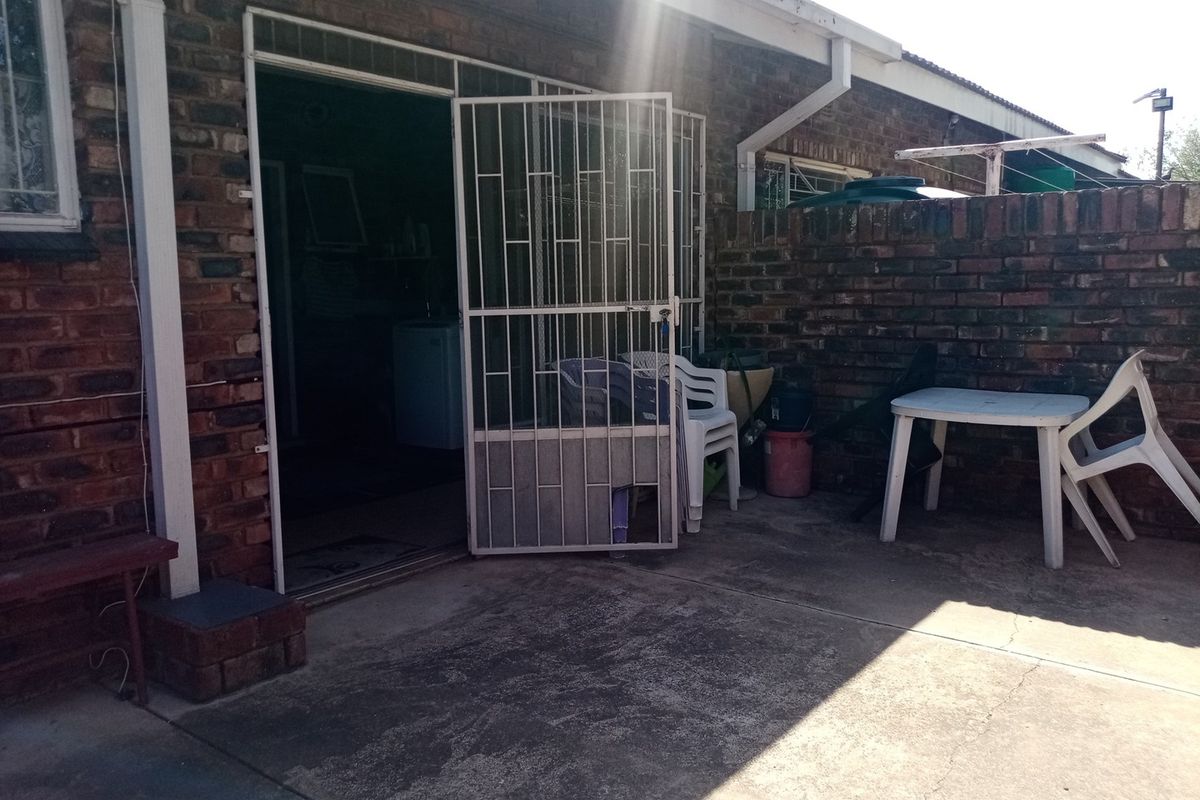 Rear exterior view of the townhouse featuring a concrete patio area, brick facade, and a security gate entrance.