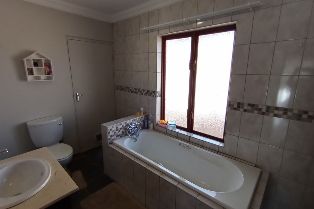 A functional bathroom featuring a built-in bathtub with tiled surround, a vanity basin, and a toilet, finished with neutral wall tiles.