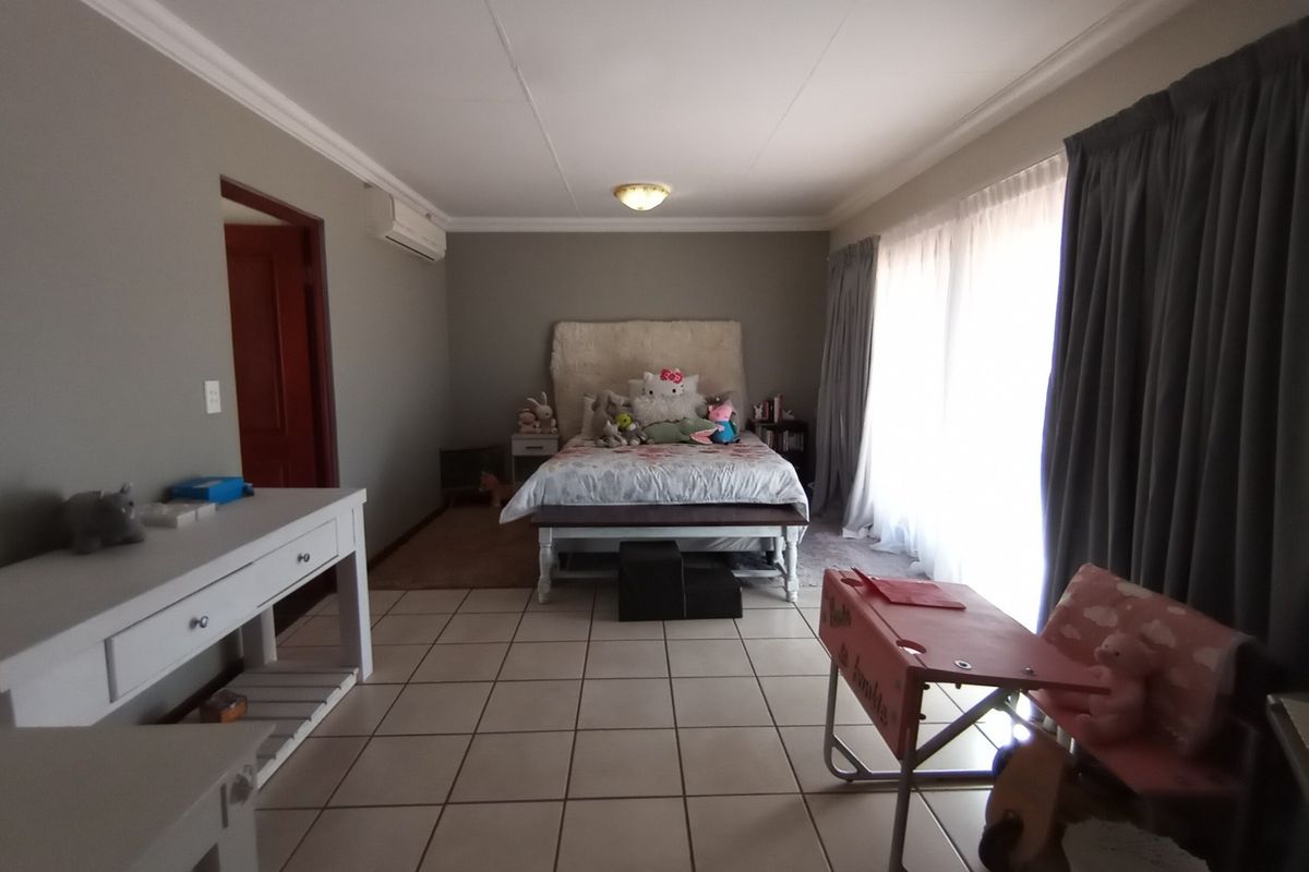 Spacious bedroom featuring tiled flooring, a wall-mounted air conditioning unit, and large windows with curtains, providing ample natural light.
