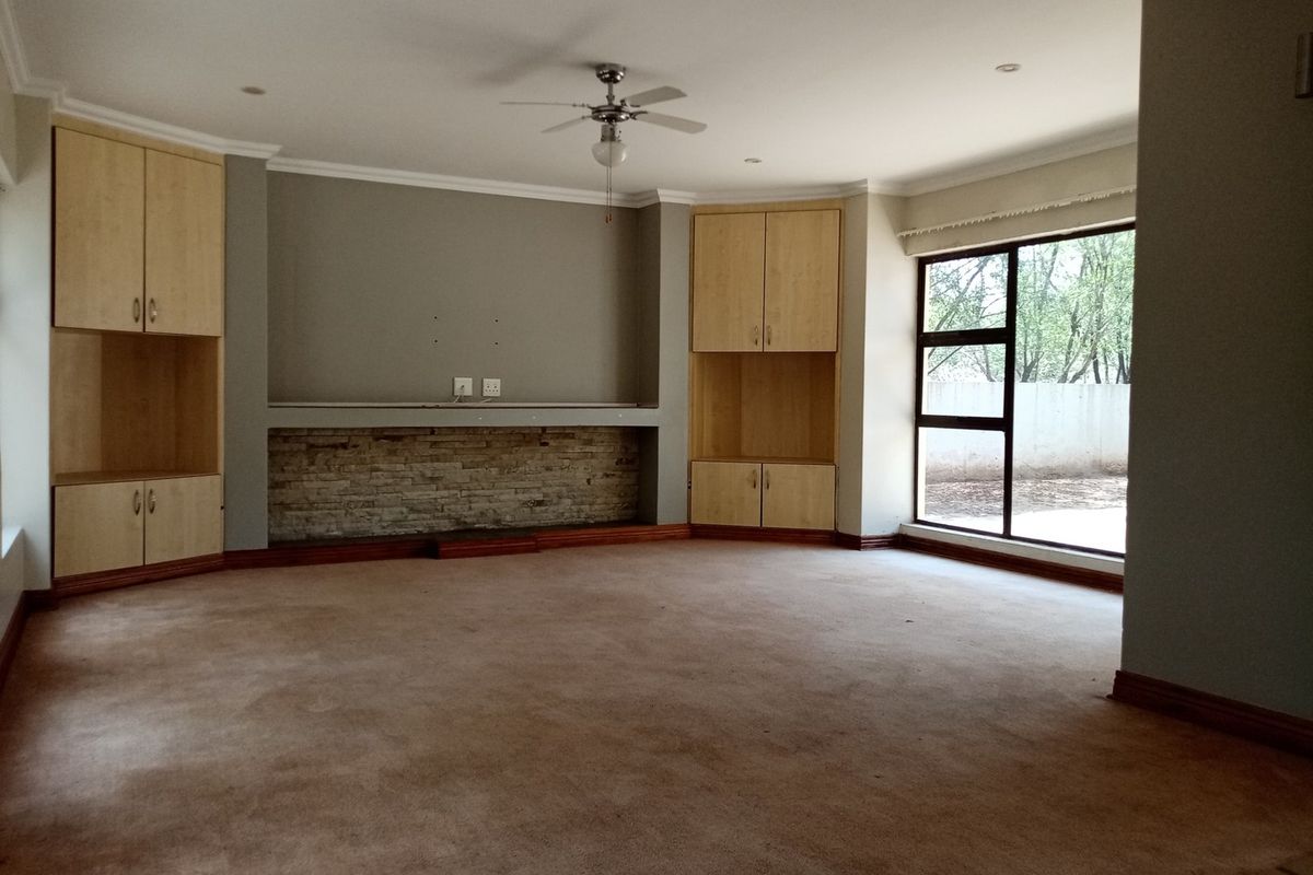 Spacious living room featuring built-in wooden cabinetry, a stone-clad feature wall, ceiling fan, and large windows providing natural light.