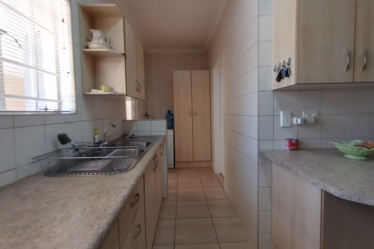A functional kitchen featuring laminate countertops, built-in cabinetry, a double stainless steel sink, and tiled flooring with neutral wall tiles.
