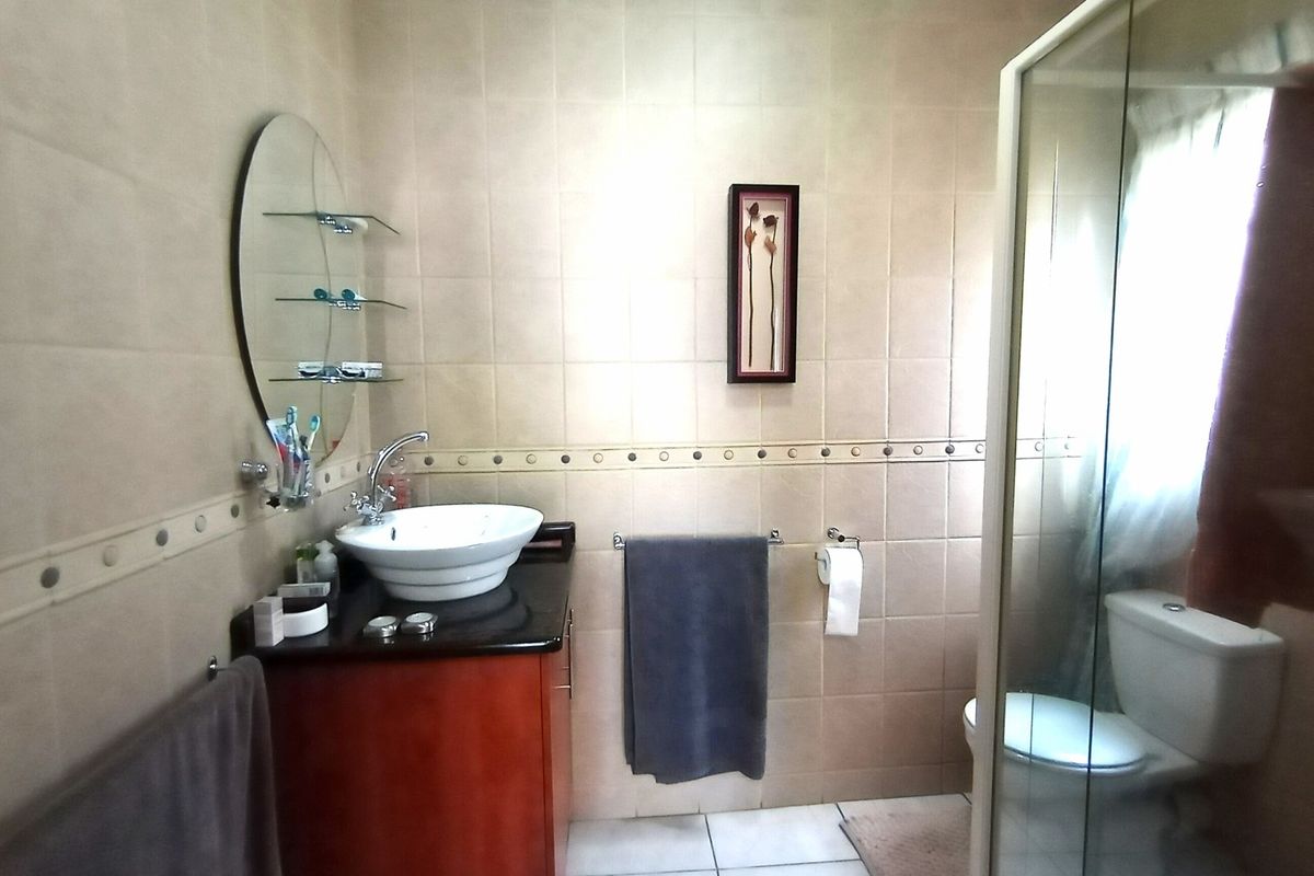 A functional bathroom featuring a vessel sink vanity, a glass-enclosed shower, and neutral wall tiling.