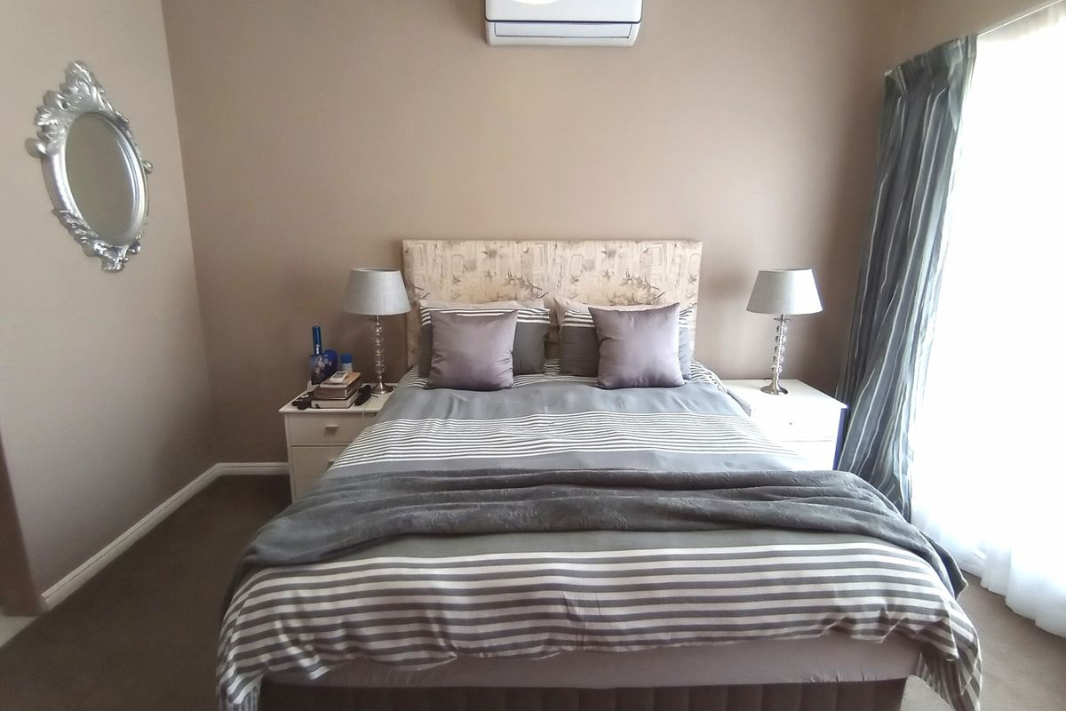 A well-maintained bedroom featuring neutral wall tones, carpeted flooring, and a wall-mounted air conditioning unit.