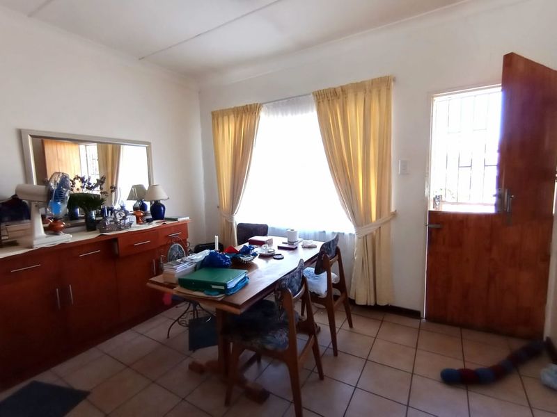 A dining room featuring tiled flooring, a wooden entrance door with a security gate, and a large window allowing natural light.