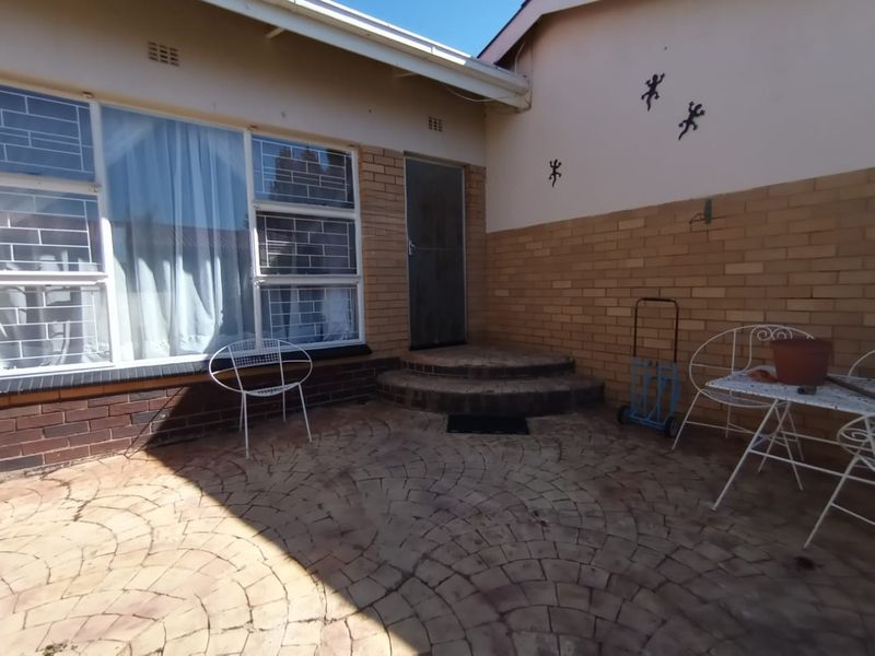 A rear patio area featuring patterned brick paving, a stepped entrance, and brick wall finishes with security-barred windows.