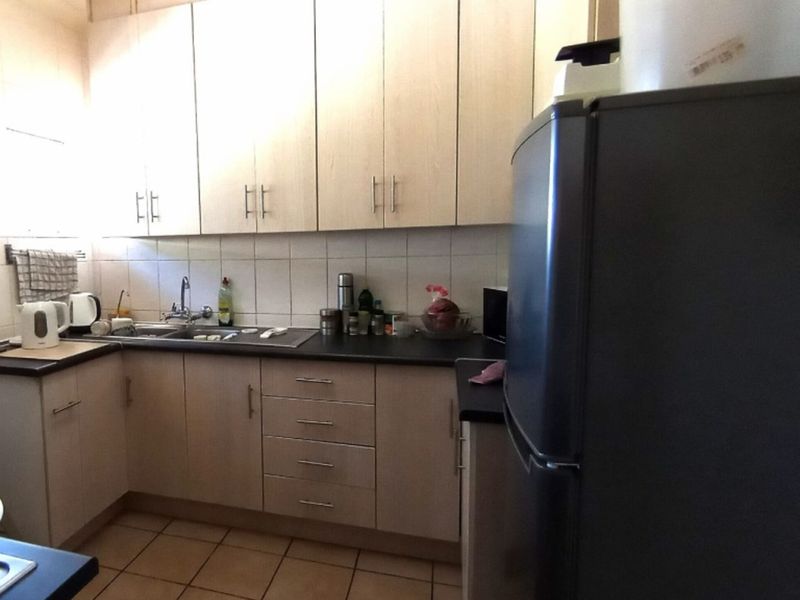 A functional kitchen featuring light-toned laminate cabinetry, dark countertops, tiled backsplash, and ceramic floor tiles, offering a practical layout for daily use.