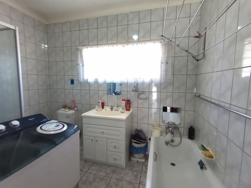 A functional bathroom featuring a vanity cabinet, bathtub, and separate shower enclosure with full-height wall tiling and a wall-mounted drying rack.