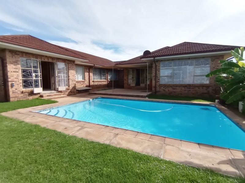 Spacious rear garden featuring a large swimming pool, paved surround, and brick house exterior with security gates.