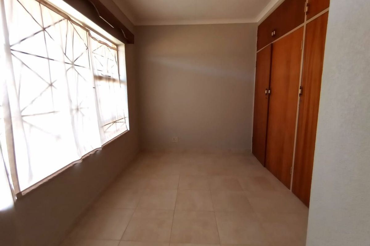 A vacant bedroom featuring tiled flooring and built-in wooden cupboards, offering a clean and neutral space ready for personalization.