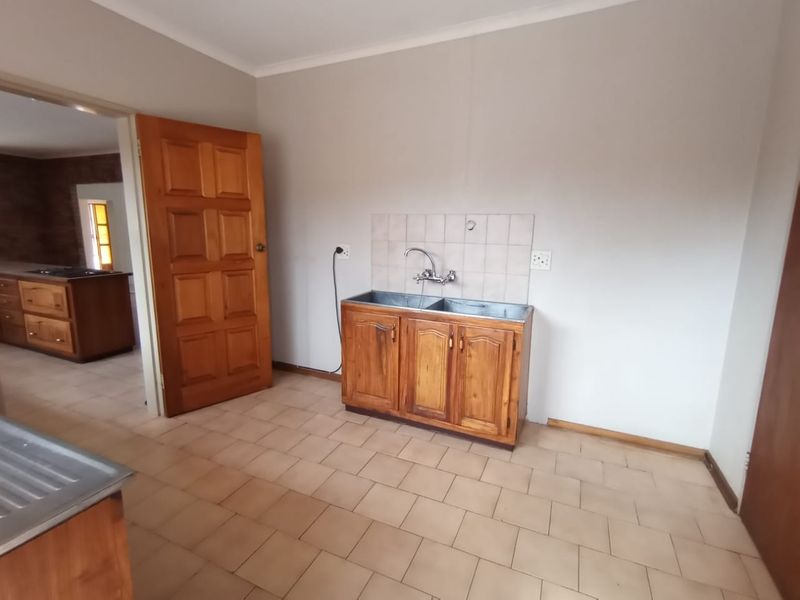 A functional laundry area featuring a double basin sink, wooden cabinetry, and tiled flooring, providing a practical space for utility and washing needs.
