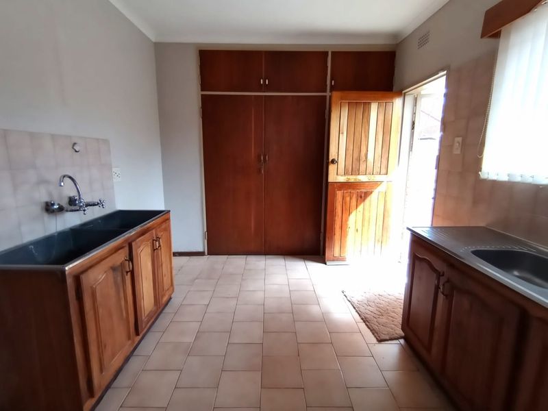 A functional laundry room featuring built-in wooden cabinetry, double basin sink, tiled flooring, and direct access to the exterior via a stable door.