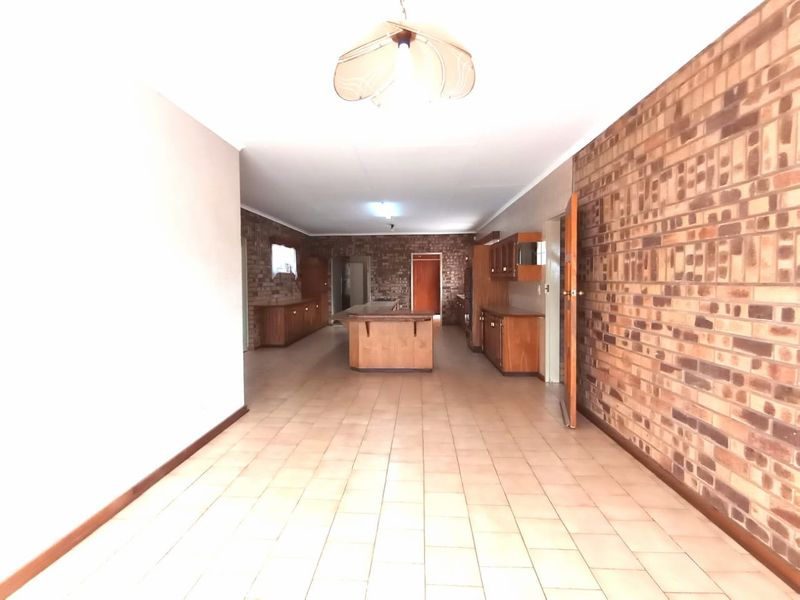Spacious open-plan kitchen area featuring extensive built-in wooden cabinetry, a central island, and a prominent exposed brick wall with ceramic tile flooring.