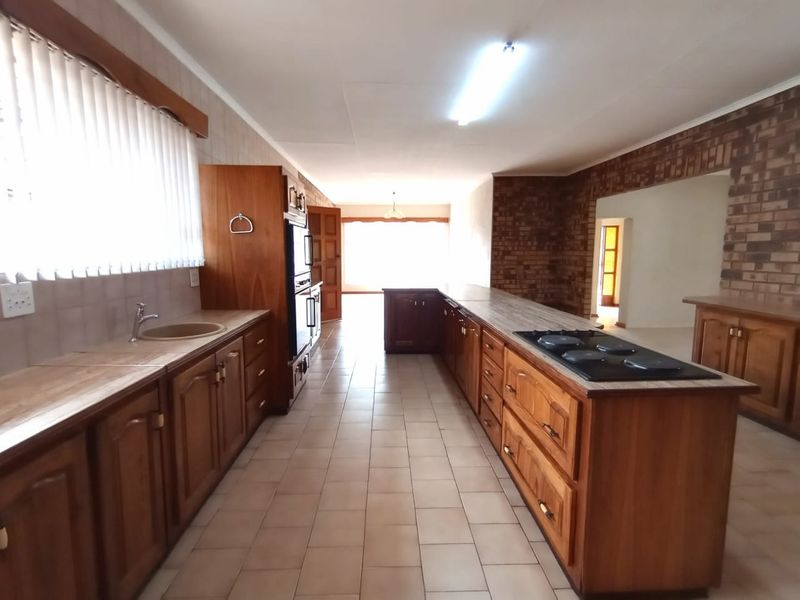 Spacious kitchen featuring extensive wooden cabinetry, built-in oven and hob, tiled flooring, and an exposed brick feature wall.