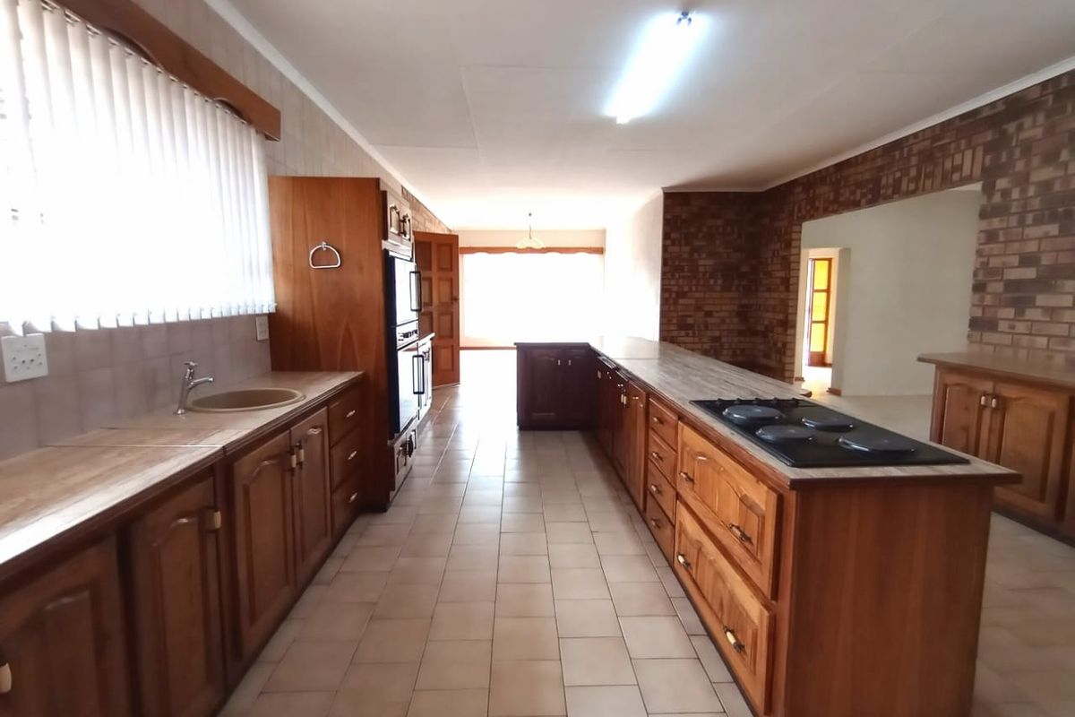 Spacious kitchen featuring extensive wooden cabinetry, built-in oven and hob, tiled flooring, and an exposed brick feature wall.