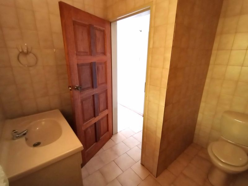 A dated bathroom featuring a vanity basin, toilet, and neutral wall and floor tiling, presenting an opportunity for modernization.